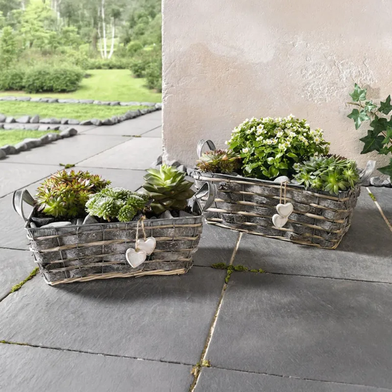 Die beiden Pflanzer im zweier Set sind aus Zink gefertigt und mit seitlichen Griffen versehen. Außen sind sie aufwändig beflochten und von grau gekalkter Birkenrinde und Spaltweide umgeben. Sie sind mit jeweils zwei kleinen Holzherzen in zeitlosem weiß liebevoll dekoriert.