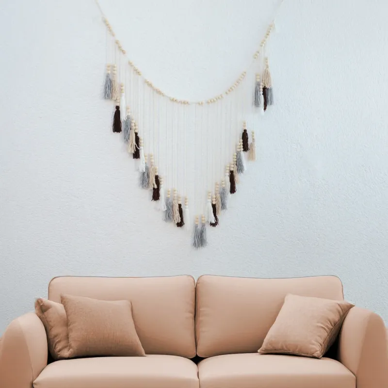DECCARO Makramee Girlande Tassel. Kombination aus naturfarbenem Baumwollseil mit kleinen Holzperlen und vom Baumwollseil nach unten hängenden Baumwollquasten in den Farben weiß, beige, grau und braun. Oberhalb der Quasten befinden sich an jeder Quaste je drei Holzperlen.