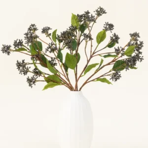 Ein künstlicher Seidenblumenstrauß „Japanese Berry Steel Blue“ mit langen Stielen, dunkelvioletten Beeren und Stahlblättern steht in einer Vase mit weißer Textur vor einem schlichten hellen Hintergrund.
