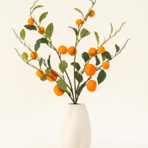 Der künstliche Blumenstrauß „Mandarin“ aus Seide besteht aus einer weißen, strukturierten Vase und Zweigen aus grünen Blättern und leuchtend orangefarbenen künstlichen Mandarinen, die vor einem schlichten, hellen Hintergrund eine lebendige Note verleihen.