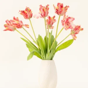 Eine Vase mit weißer Struktur zeigt den Seiden-Kunstblumenstrauß French Parakeet Tulip rot/gelb mit naturgetreuen roten und gelben Tulpen mit grünen Blättern vor einem schlichten hellen Hintergrund.
