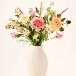 In einer weißen Keramikvase befindet sich der Strauß „Backyard Blossom“ aus künstlichen Seidenblumen, bestehend aus einem wunderschönen Arrangement aus rosa Rosen, weißen Gänseblümchen und kleinen gelben Blüten aus Seidenblumen, ergänzt durch üppige grüne Blätter vor einem schlichten hellen Hintergrund.