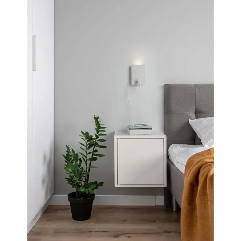 Zen LED Wandleuchte mit Lesearm & USB an einer Wand neben dem Bett und einem Nachttisch mit Pflanze.