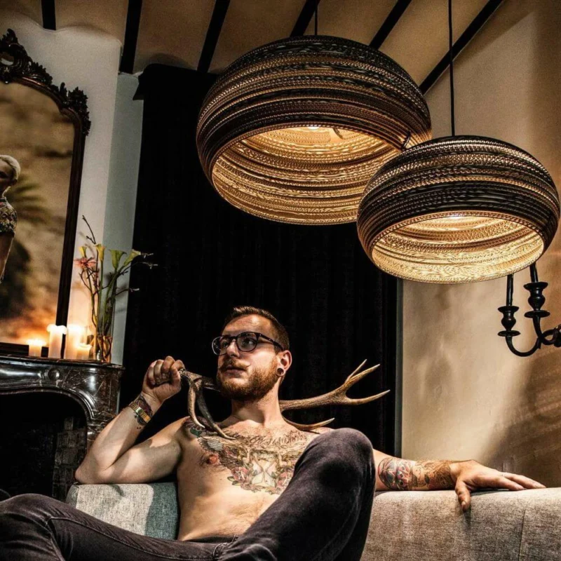 Dandy Pendellampe aus Karton oval im modernen Wohnraum mit einem Mann und stilvollem Interieur.
