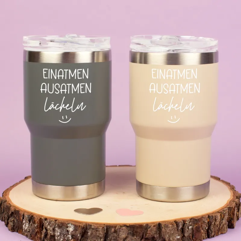 Zwei Thermobecher in Grau und Beige mit Spruch Einatmen Ausatmen Lächeln auf Holzscheibe dekoriert