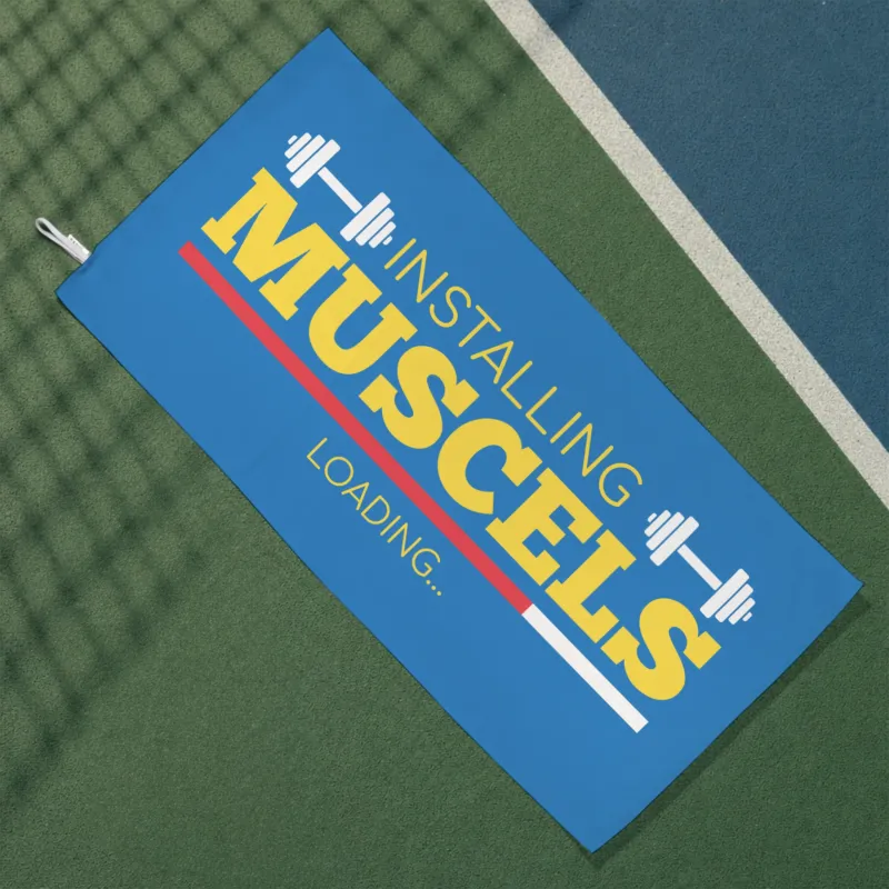 Blaues Gym Handtuch mit Hantelmotiv und Installing Muscles Loading Schriftzug auf Sportplatz