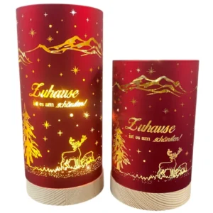 Zwei rote Deko-Lichter mit goldener Winterlandschaft und dem Schriftzug „Zuhause ist es am schönsten!“, auf hellem Holzsockel