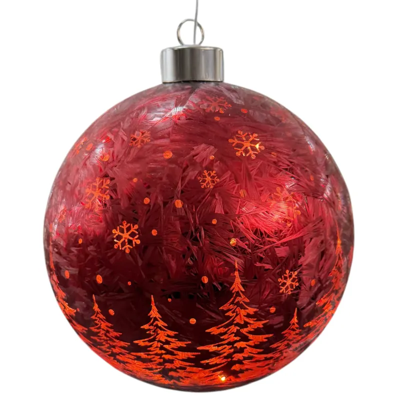 Rot leuchtende Kugeldekoration mit Tannenbaum- und Schneeflockenmuster vor verschneiter Fensterkulisse.