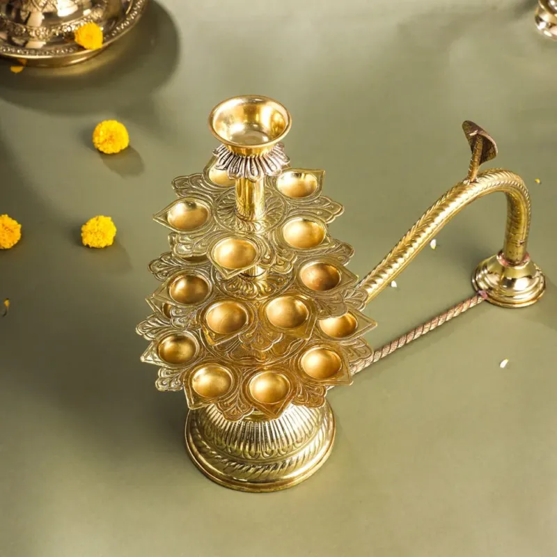 A brass traditional Ganga aarti with a gold-colored handle and a round, gold-colored dish on top.