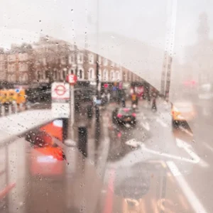 London, England I View of a rainy street through the fogged window of a legendary red London bus capturing nostalgic atmosphere photography and vibrant colors of the city in the rain with grey moody aesthetic