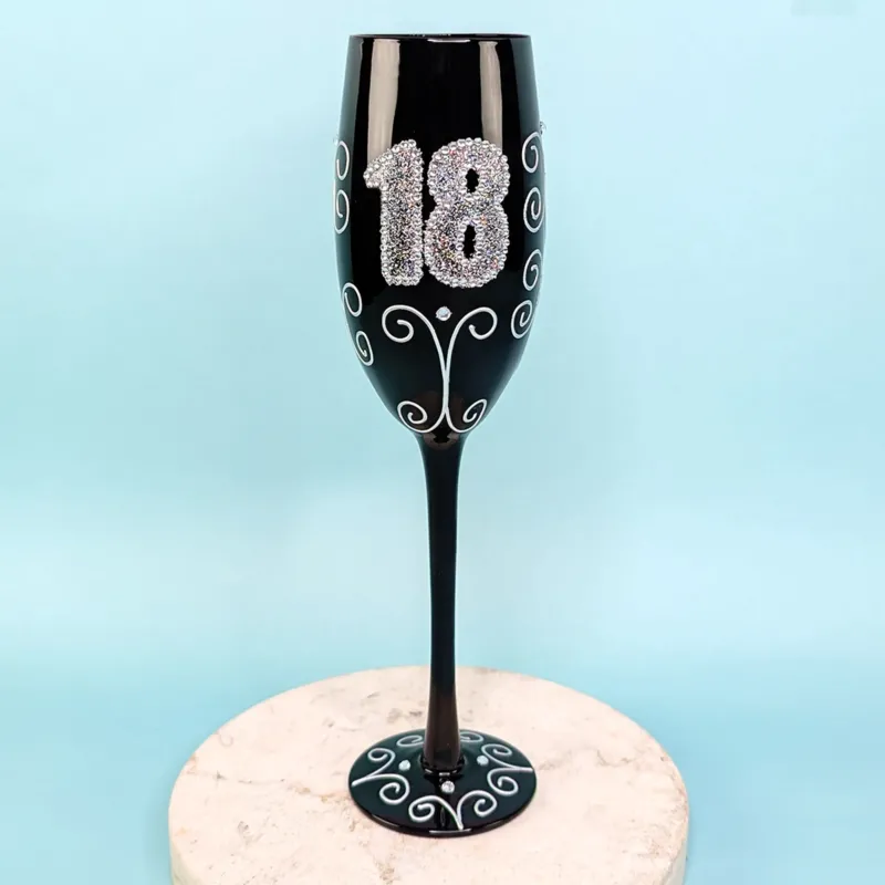 Schwarzes Sektglas mit glitzernder 18 und Ornamenten, frontal fotografiert