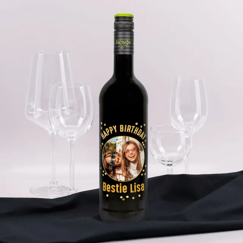 Weinflasche mit personalisiertem Etikett „Happy Birthday Bestie Lisa“ und Foto von zwei lachenden Frauen, umgeben von Weingläsern.