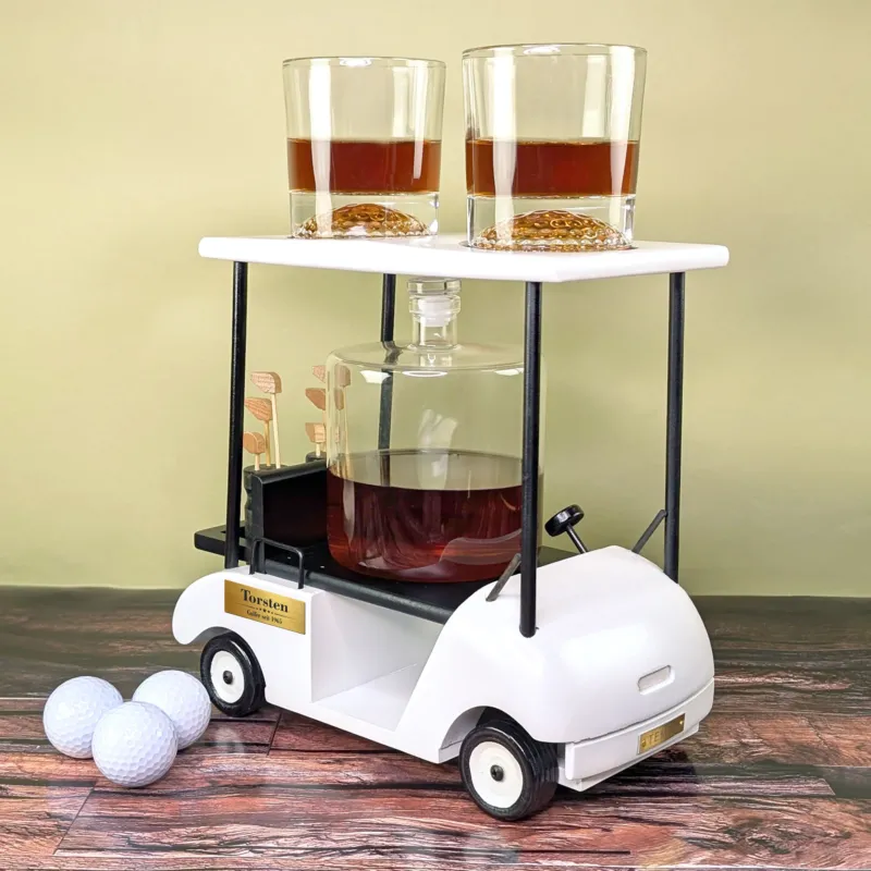 Golfcart-Whiskyset mit befüllten Gläsern und Karaffe auf dunklem Holz mit Golfbällen