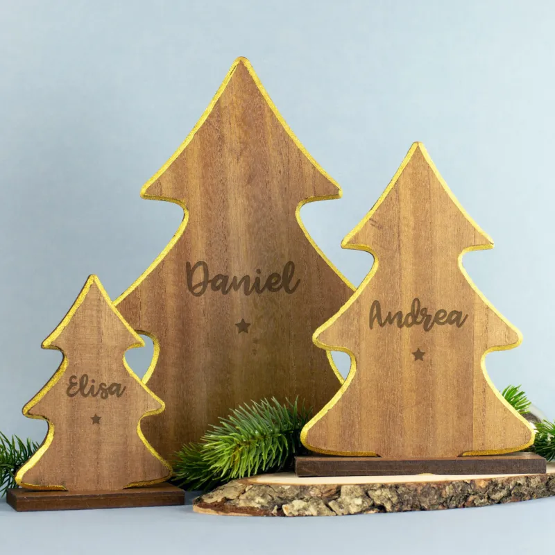 Drei weihnachtliche Holz-Tannenbäume in verschiedenen Größen mit goldfarbenem Rand und gravierten Namen „Elisa“, „Daniel“ und „Andrea“, jeweils mit kleinem Sternsymbol unter der Gravur, auf Holzsockeln stehend und mit Tannenzweig dekoriert.