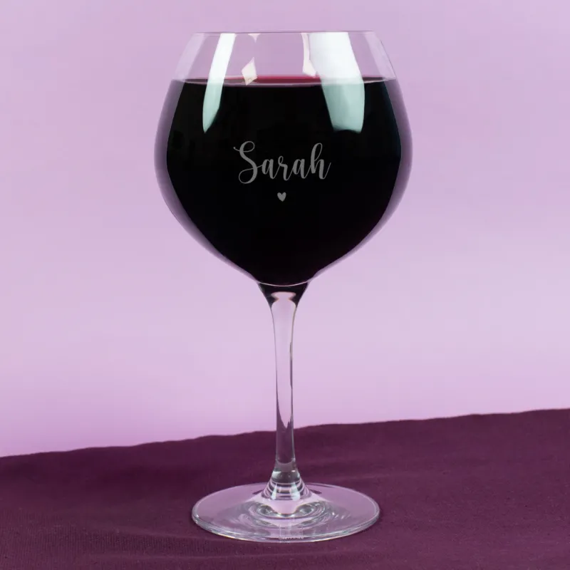 Personalisierte Gravur auf Leonardo Burgunderglas mit Name „Sarah“ und kleinem Herzmotiv – gefüllt mit Rotwein, vor pastellfarbenem Hintergrund, edel und romantisch gestaltet.