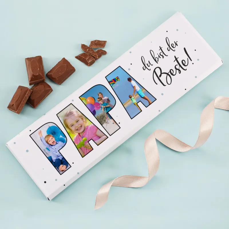 XXL Schokoladentafel „Papa du bist der Beste!“ mit 4 personalisierten Fotos und Milchschokolade-Stücken daneben auf hellblauem Hintergrund